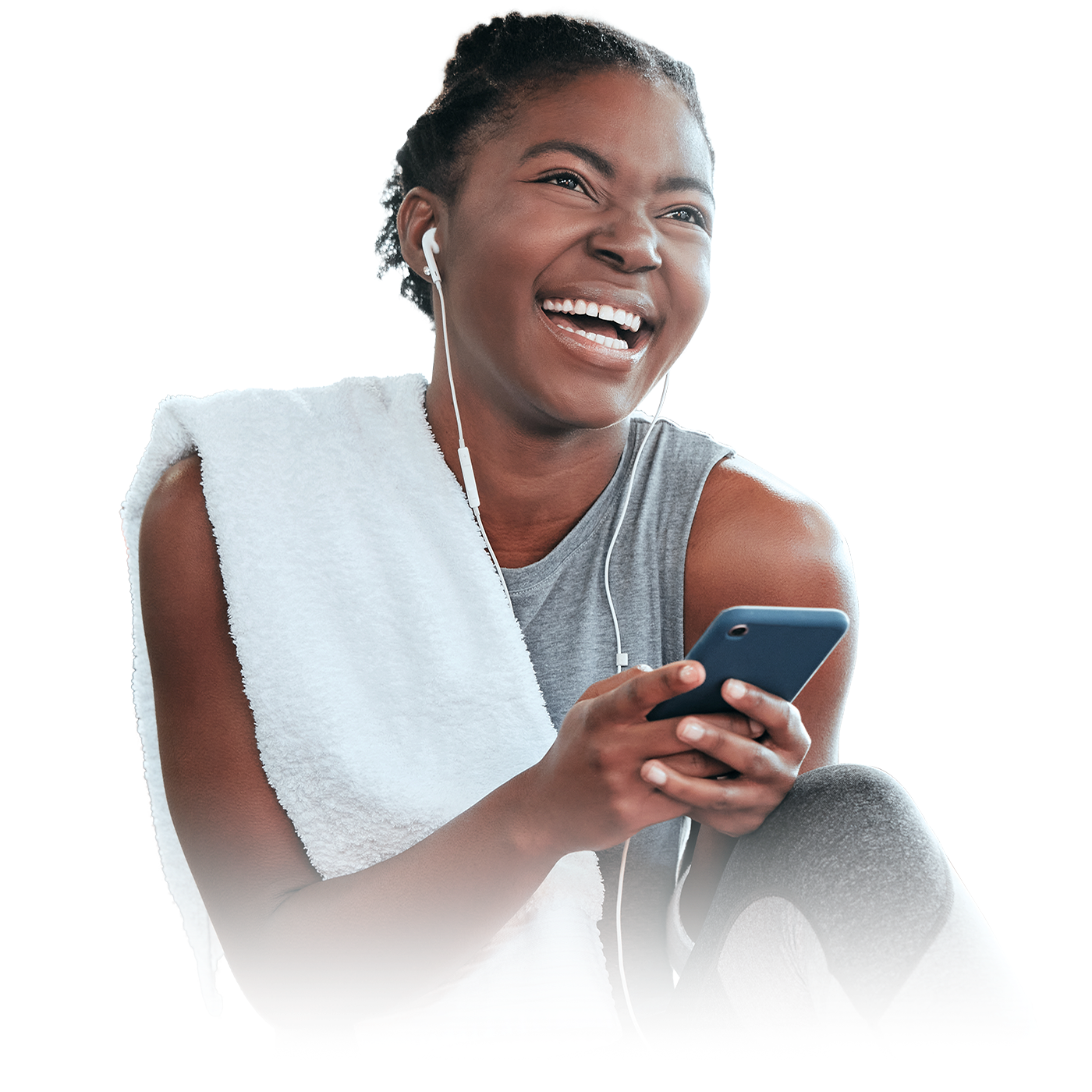 A woman in a gray top with a white towel on her shoulder, laughing with earphones connected to a phone in her hand.