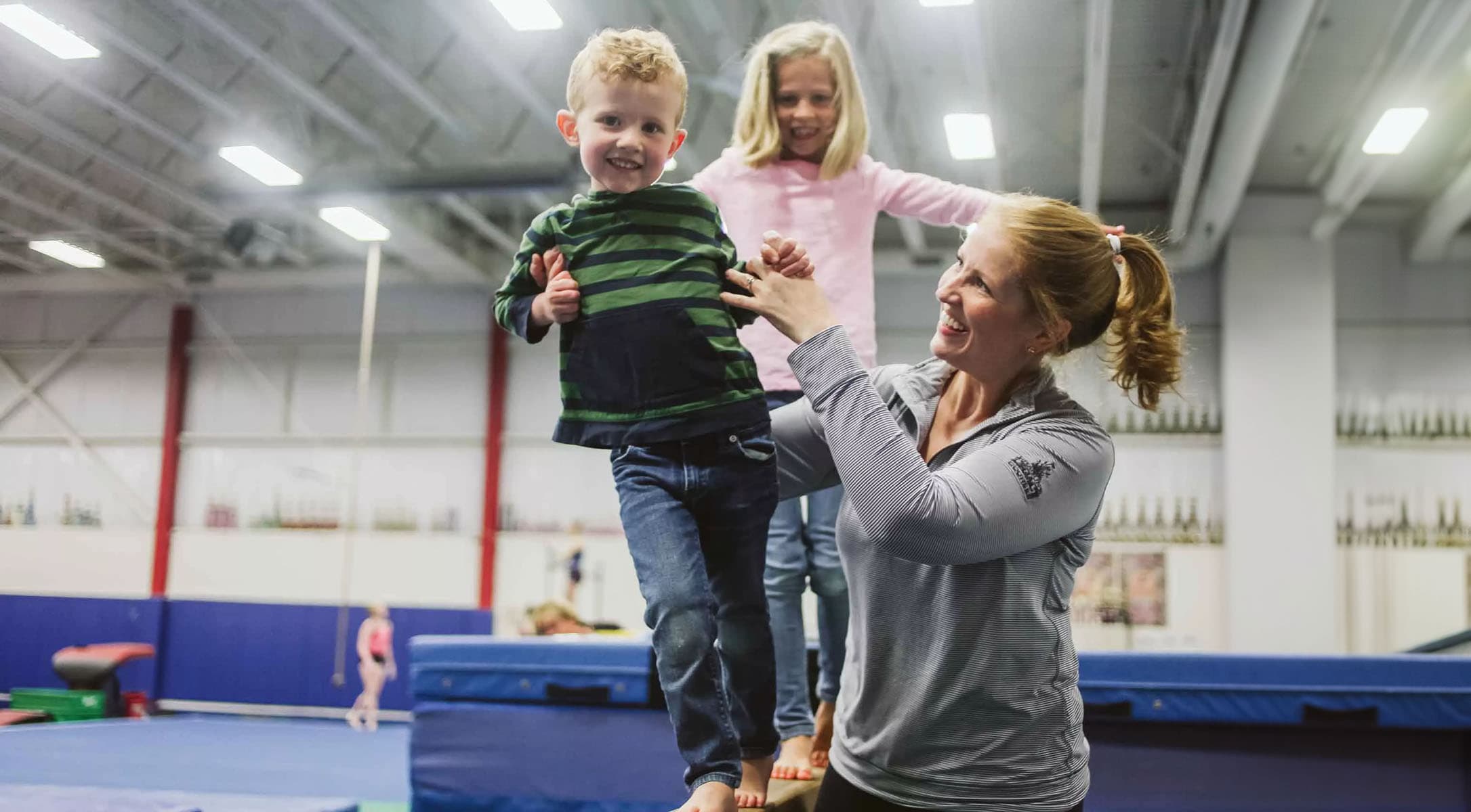 A coach assisting kids in balancing on a Gymnastic platform at a YMCA.