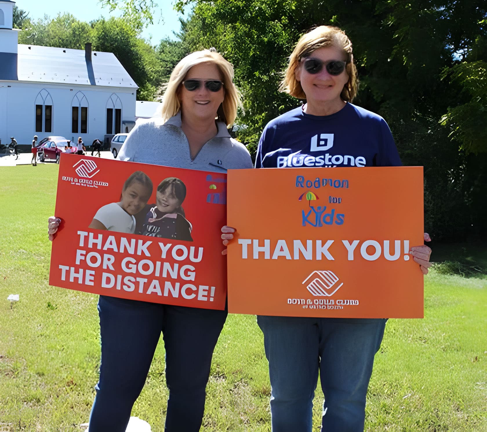 Two women holding a "thank you" board for donations raised via Daxko's fundraising software for nonprofits.