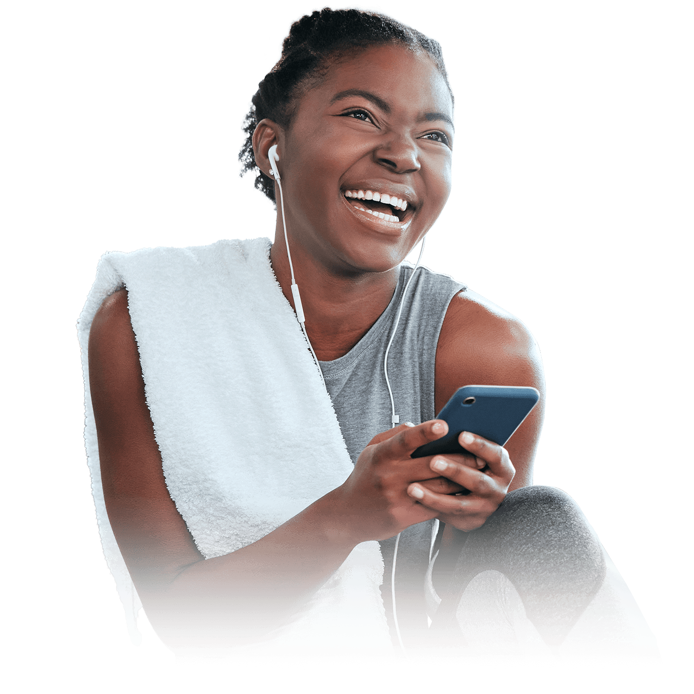 A woman in a gray top with a white towel on her shoulder, laughing with earphones connected to a phone in her hand.