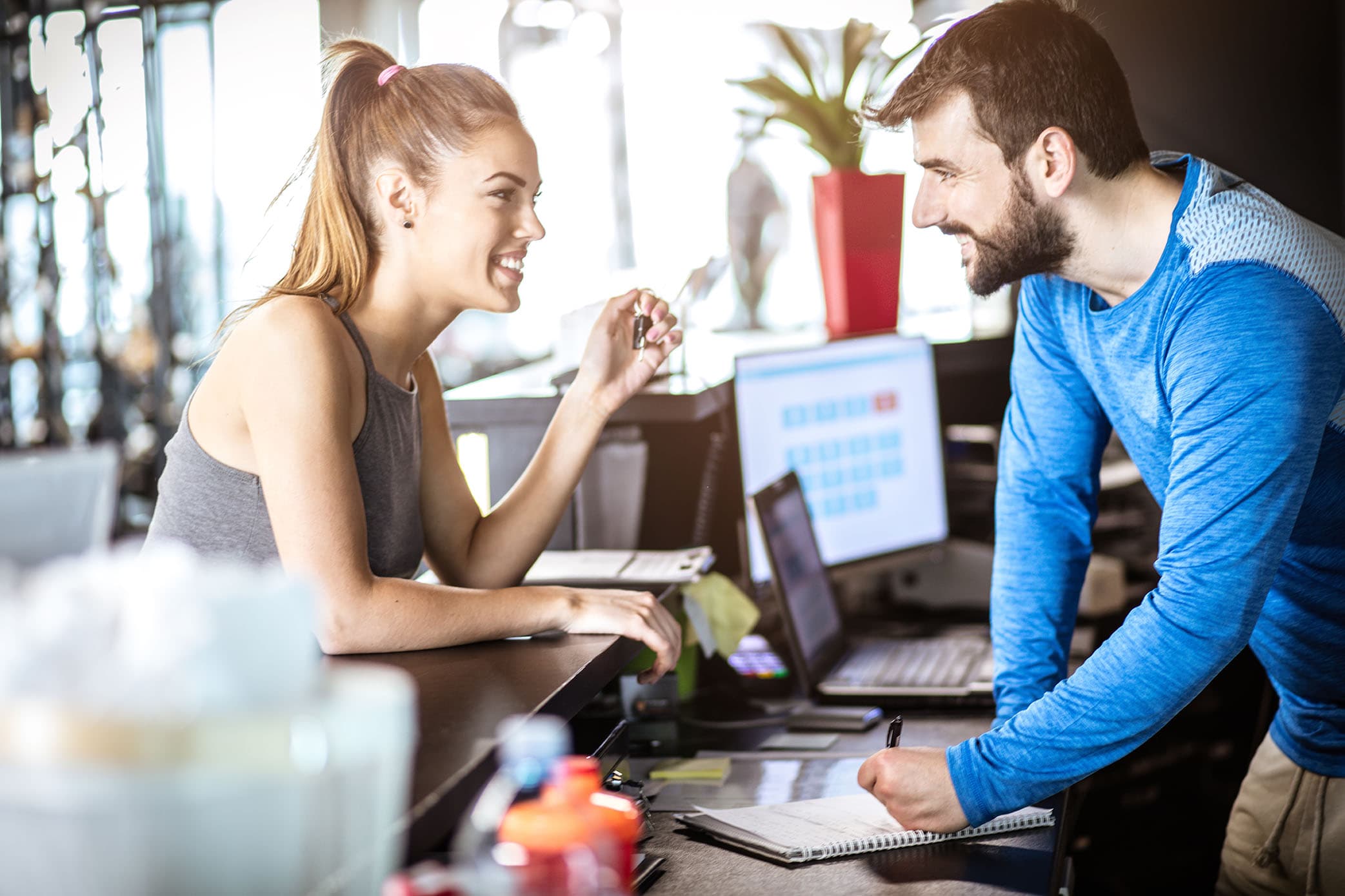 A woman checking in at the gym/club reception and having a conversation.