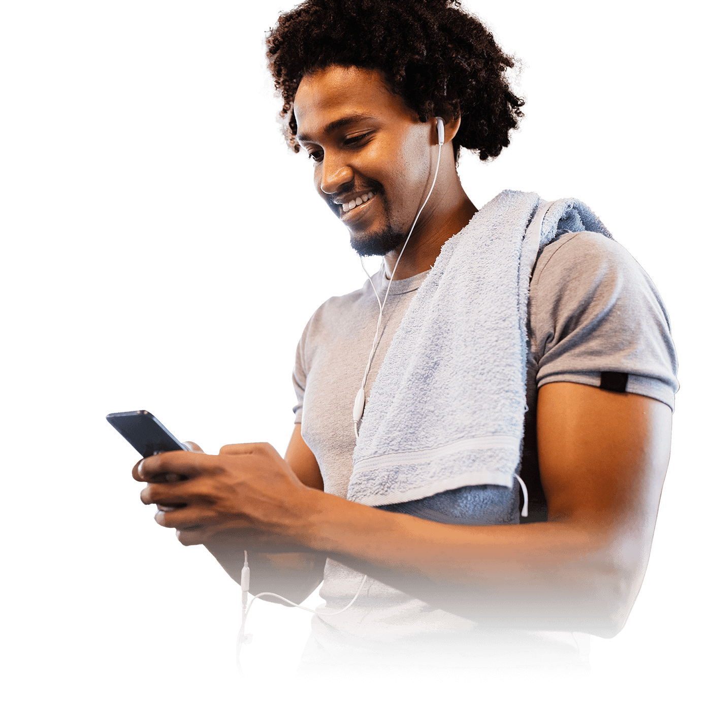 A man in a gray t-shirt with a towel over his shoulder, holding a phone with earphones plugged in.